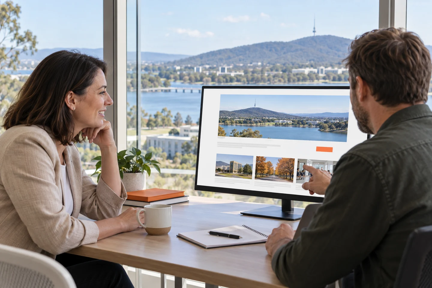 AI-generated photo showing A Canberra association manager reviewing a clear, high-contrast website layout with a web developer, the lake and Black Mountain through the window