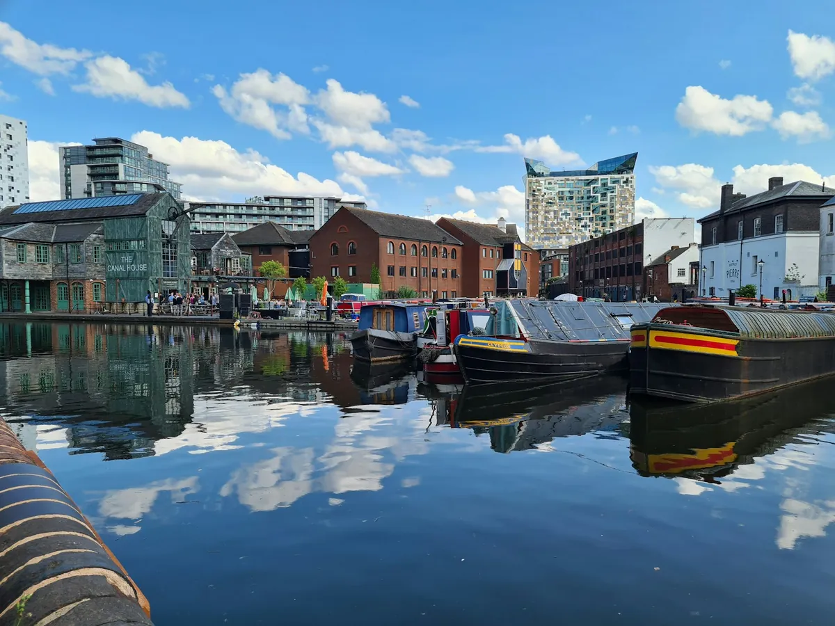 Narrowboats moored in Gas Street Basin in Birmingham with The Cube behind the brick wharf buildings