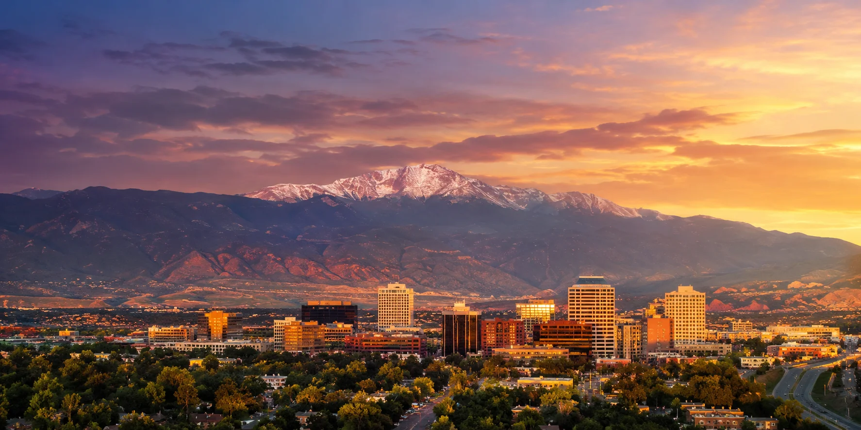 A city at the foot of a snow-capped mountain under a sunset sky