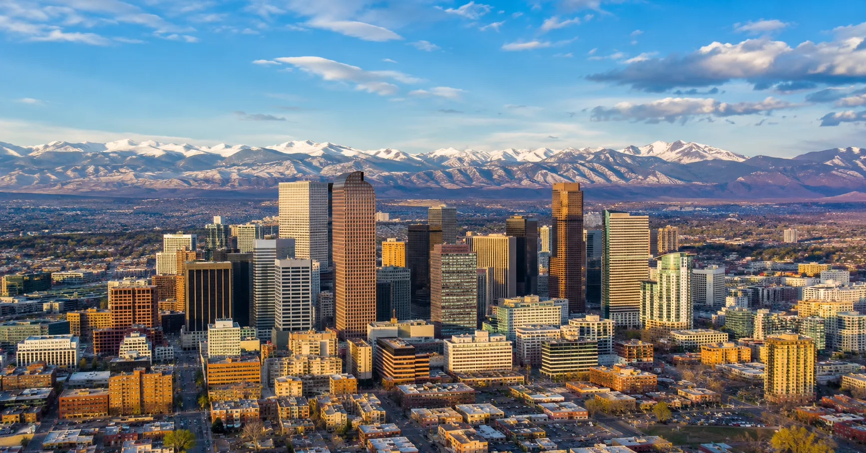Aerial view of the downtown Denver skyline with the Rocky Mountains behind it
