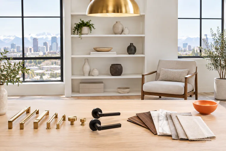 Brass cabinet pulls, black door levers and wood, marble and fabric samples on a showroom table, with the Denver skyline and mountains in the window
