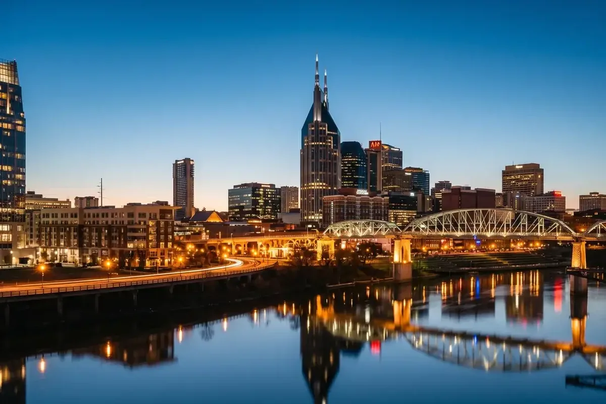 A city skyline at dusk reflected in a river, with a lit bridge