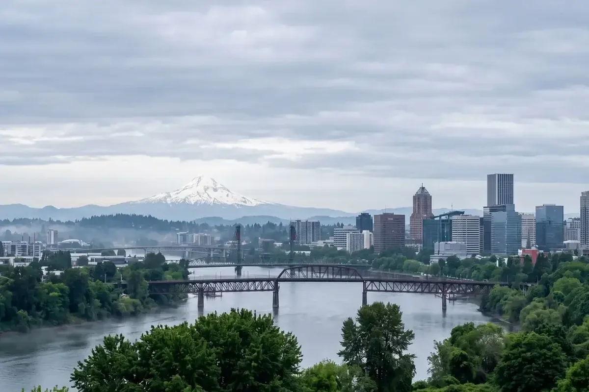 A riverside city skyline with steel bridges and a snow-capped peak behind it